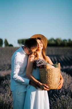 Çift, gün batımında sakin bir akşam ışığında sepetle lavanta tarlasında yürüyor.