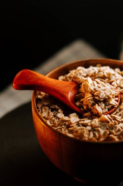 Tahta kaşıkla bir kase yulaf ezmesi sabah ışığında karanlık bir masada duruyor.