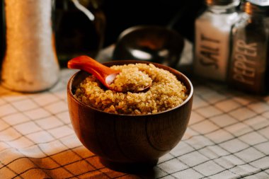 Bulgur, arka planda tuz ve yağ bulunan bir masanın üzerindeki ahşap bir kasede inliyor.