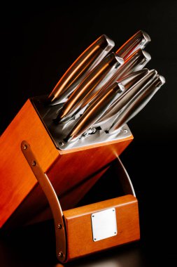 Bıçak, mutfak düzeninde koyu bir arka planı olan tahta bir bloğa yerleştirilmiş.