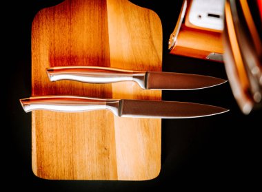 Ahşap kesme tahtasına yerleştirilmiş iki mutfak bıçağı ve parlak bir ışık.