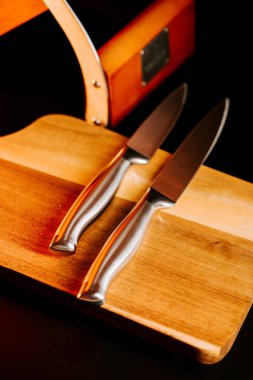 Bir kutunun yanındaki tahta kesme tahtasına yerleştirilmiş iki parlak mutfak bıçağı.