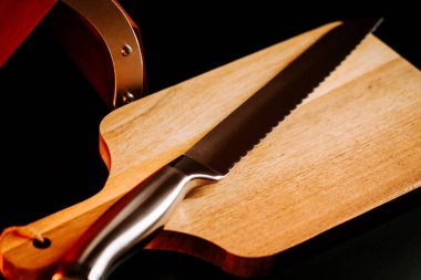 Keskin bir bıçak, tahta bir kesme tahtasına yerleştirilir. Mutfak ortamında karanlık bir arka plana yerleştirilir.