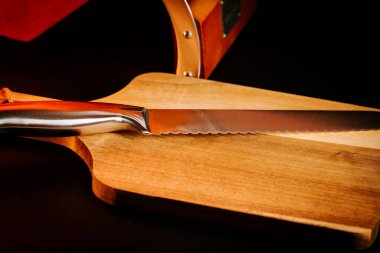 Mutfak saatinde arka planda mutfak aletleri olan tahta bir kesme tahtasındaki bıçak.