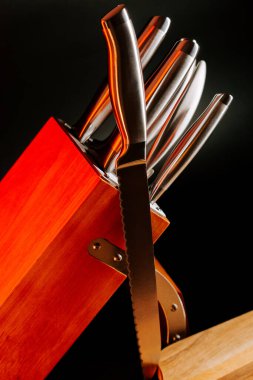 Tahta bir bloktaki bıçaklar, üzerine yaslanmış bir bıçakla karanlık bir arka plan.