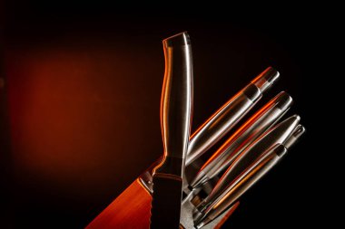 Bıçak bloğu, parlak bıçaklarla karanlık ortamda, ahşap bir zemine yerleştirilmiş.