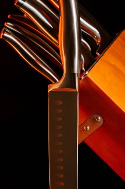 Mutfak bıçağı ve bıçak bloğunun karanlık bir ortamda parlayan aletleriyle yakın görüntüsü