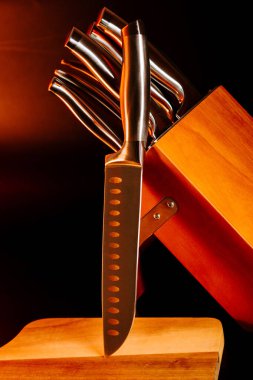 Koyu arkaplanı olan tahta kesme tahtasındaki bir blokta bıçaklar.