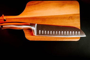 Keskin mutfak bıçağı, karanlık bir ortamda tahta bir kesme tahtasına yerleştirilmiş.