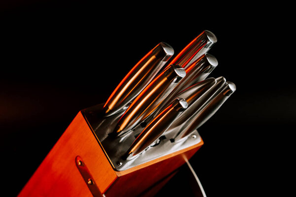 Острые кухонные ножи в деревянном блоке помещены на темном фоне с мягким светом