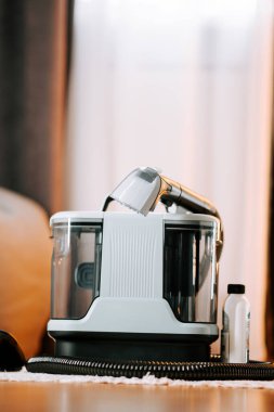 Parlak bir odada elektrikli süpürgeyi temizlerken pencereden içeri ışık giriyor.