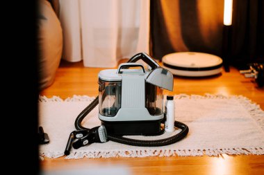 Evinde ahşap zemini olan geniş bir odada beyaz bir halıda elektrikli süpürge yıkamak.