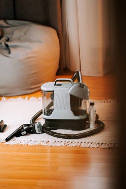Evdeki temizlik sırasında kanepenin yanındaki halının üzerine yerleştirilmiş elektrikli süpürge.