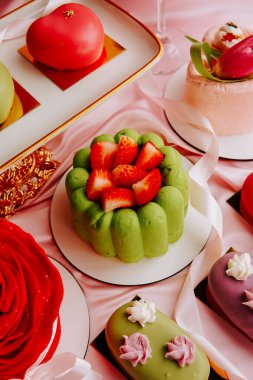 Çeşitli tatlılar pembe kumaşlı bir masaya dizilmiştir.