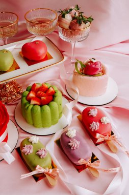 Bir partide pembe kumaş, meyve ve dekoratif öğelerle dolu bir masada renkli tatlılar.