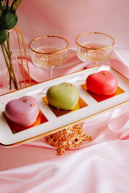 Kutlama sırasında yumuşak pembe bir ortamda gözlüklü, süslü bir tepside kalp şeklinde ikramlar.