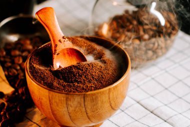 Kahve ahşap bir kasede, mutfak masasında bir kaşık ve kahve çekirdekleri arkasında duruyor.