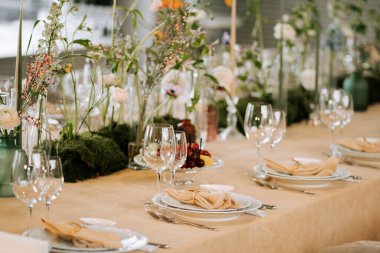 Bir etkinlik için çiçekler, tabaklar ve bardaklarla hazırlanmış zarif bir yemek masası.