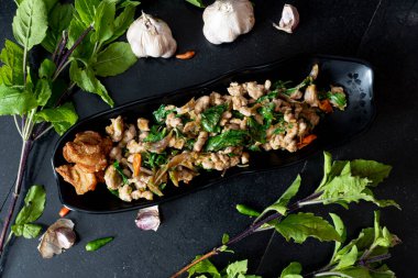 Kızarmış domuz fileto ve domuz etli baharatlı fesleğen. Siyah bir tabağa koy. Fesleğen, sarımsak ve biberli siyah fayansla döşenmiş.