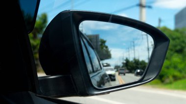 Arabanın soyut ayna görüntüsü. Arkalarında birkaç arabayla seyahat etmek için geriye bakıyorlar. Mavi gökyüzü ve elektrik direğinin altında yeşil ağaçlar olan yol kenarı.