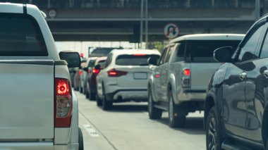 Beyaz pikap durağının arka tarafında fren lambası açık. Arabalar trafik ışıklarının önüne dizildi. İleride kavşağın üzerinde bir köprü var. Beton yolda trafik sıkışık..