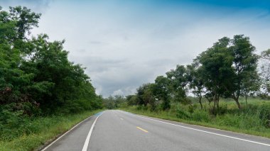 Asphalt yolu ilerideki hedefe gidiyor. Yolun iki tarafında ağaçlar ve yeşillikler var. Mavi gökyüzü ve beyaz bulutların altında. Turizm için açık yollar.