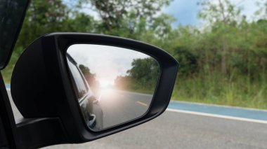 Asfalt yolda araba sürerken ayna görüntüsü. Bisiklet için bulanık çizgili yol kenarı. Aynadaki yansıma, boş bir yoldan, arabanın arkasından ve parlak ışıktan oluşur..