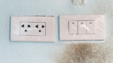 Üç düğmeli yeni elektrik prizi. Plastiğe sarılıp sarmalanmadığını kontrol et. Eski beton duvarın üzerinde mavi lekeli.