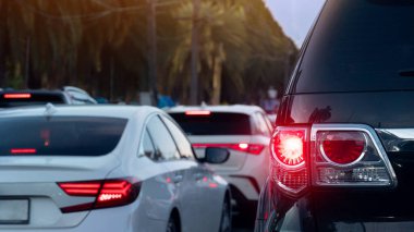 Lüks arabanın arka tarafında fren lambası açık. Trafik sıkışık ve bir sürü araba kuyruğu var. Arkaplan için uzun ağaçların bulanıklığı.