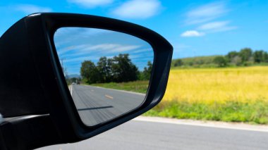 Aynada asfalt yolu gölgesi olan araba aynası. Altın pirinç tarlaları manzaralı aspahlt yolda araba yolculuğu. Tayland 'ın kırsal tarım alanları.