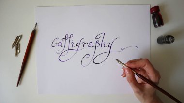 Kalem ve mürekkep şişeleri kullanarak beyaz kağıda mürekkeple el yazısı yazmak. Kafkasyalı bir kadının eli. Sanat, yaratıcılık, geleneksel yazı, zanaat ve zarif tasarım kavramı.