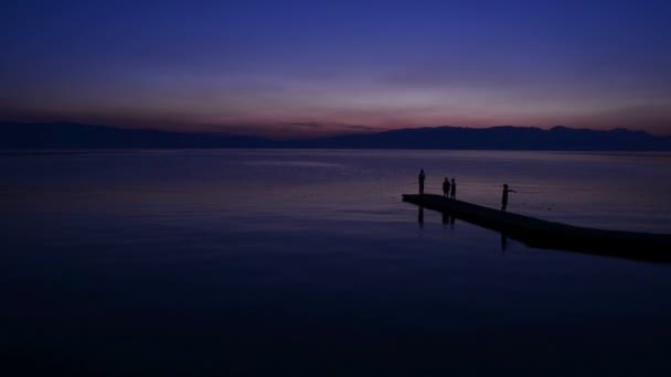 Menschen genießen Sonnenuntergang am ruhigen See — Stockvideo
