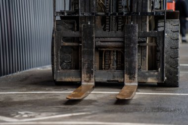 Görünür çelik kaldırma çatalları ve ağır lastikleri olan forkliftin önü. Deponun zemininde duruyor. Endüstriyel makine detaylarını gösteriyor.