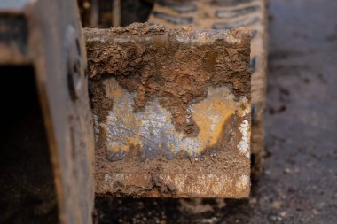 Çamurla kaplı kazıcı bıçağının yakın çekimi, inşaat alanındaki çalışmalardan sonra kaba doku, çelik yüzey ve toprak kalıntılarını gösteriyor. Ağır toprak hareket makinelerini temsil ediyor.