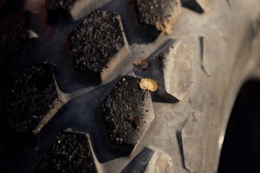Çamur tortusu ve sonbahar yapraklı ağır sanayi lastiği kalıplarının yakın çekimi, makine kullanımı için kauçuk doku ve çekiş yüzey tasarımını gösteriyor.
