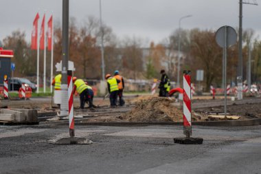 Yansıtıcı yelek giyen yol inşaat işçileri, kentsel caddede asfalt kaldırımları onarıyor. Ekip çalışması, altyapı bakımı ve şehir geliştirme sürecini gösteriyor.