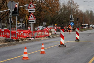 Şehir yolu görünür trafik konileri, inşaat tabelası ve belediye caddesinin yeniden inşasını ve inşaat mühendisliği operasyonlarını temsil eden yansıtıcı giysili işçiler tarafından onarılıyor.