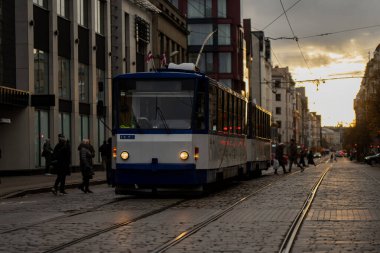 Riga şehir merkezindeki elektrik tramvayı kaldırım taşları boyunca yürüyor. Yayalar ve modern mimariyle çevrili. Sürdürülebilir toplu taşımacılık ve Baltık kentsel hareketlilik kavramını vurguluyor.