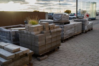 Açık hava depolama alanındaki ahşap paletlere yerleştirilmiş beton kaldırımlar ve inşaat malzemeleri, inşaat sahasına hazırlık ve kentsel altyapı planlamasını temsil etmektedir.