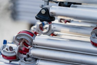 İnşaat malzemelerini, endüstriyel lojistiği, modüler çerçeve tasarımını ve kurulum hazırlıklarını temsil eden kıskaç ve konnektörlü metal yapı tüpleri yığını