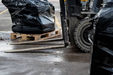 Sanayi forklifti, ambar lojistiği, ambalaj koruması, kargo taşımacılığı ve imalat veya inşaat ortamlarında ulaşım sürecini gösteren siyah ambalajlı malları paletlere yüklüyor