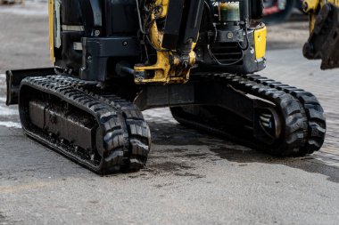 Asfalt yüzeyinde lastik izleri olan kompakt kazıcı, modern inşaat makineleri, endüstriyel mühendislik ekipmanları, zemin çalışması teknolojisi ve mekanik hareketlilik sistemini temsil ediyor.