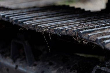 Çamurla kaplanmış kauçuk kenarları ve yükseltilmiş demirler arasında sıkışmış enkaz parçaları sürekli yer değiştirme koşullarının yol tutuş aşınmasını gösteriyor.