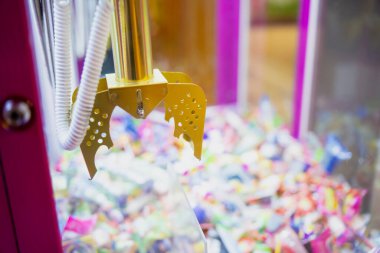 Arcade ödül makinesinin içinde asılı duran metalik bir pençenin detaylı görünümü renkli ödüllerin karışımı, etkileşimli eğlence ekipmanlarında kullanılan yakalama mekanizmasını vurguluyor