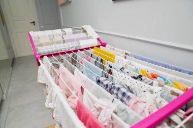 Temiz, iyi aydınlatılmış bir ev ortamında, birden fazla hat boyunca düzenlenmiş, parlak mandallarla korunan çeşitli giysiler ve havlular tutan kapalı bir çamaşır askısının geniş bir görüntüsü.