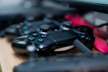 Görünür eylem düğmeleri olan siyah oyun kontrolörleri, bağlı kablo ve bulanık konsol alanı odaklı oyun ekipmanı sahnesi oluşturur