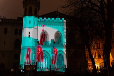 Riga tarihi binası, ışık sanat festivali sırasında turkuaz ve kırmızı projeksiyonla aydınlatıldı. Detaylı dış görünüş ile canlı mimari dönüşüm yarattı.