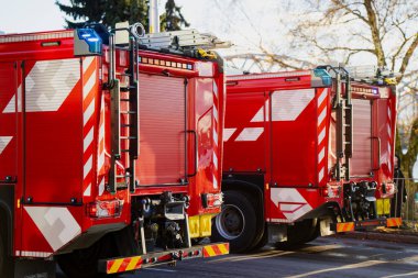 Köprü iskeleti park halindeki aracın arkasında görünürken, görünür merdivenleri, yansıtıcı grafikleri, bölme panelleri ve engebeli lastikleri olan iki itfaiye aracı yerleştirildi.