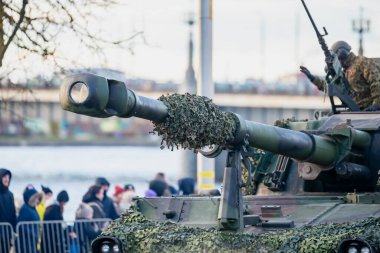 NATO savaş tankı kamufle edilmiş ana silah, taret zırhı ve taktiksel teçhizatla Müttefik Savunma Teşkilatı sırasında arka planda görünür kalabalıkla sunuldu