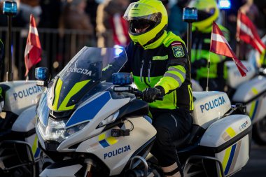 Letonya 'dan gelen kolluk kuvvetleri motosiklet birimi yüksek görüş donanımı, acil aydınlatma ve organize halk etkinliklerinde ulusal bayraklara sahip